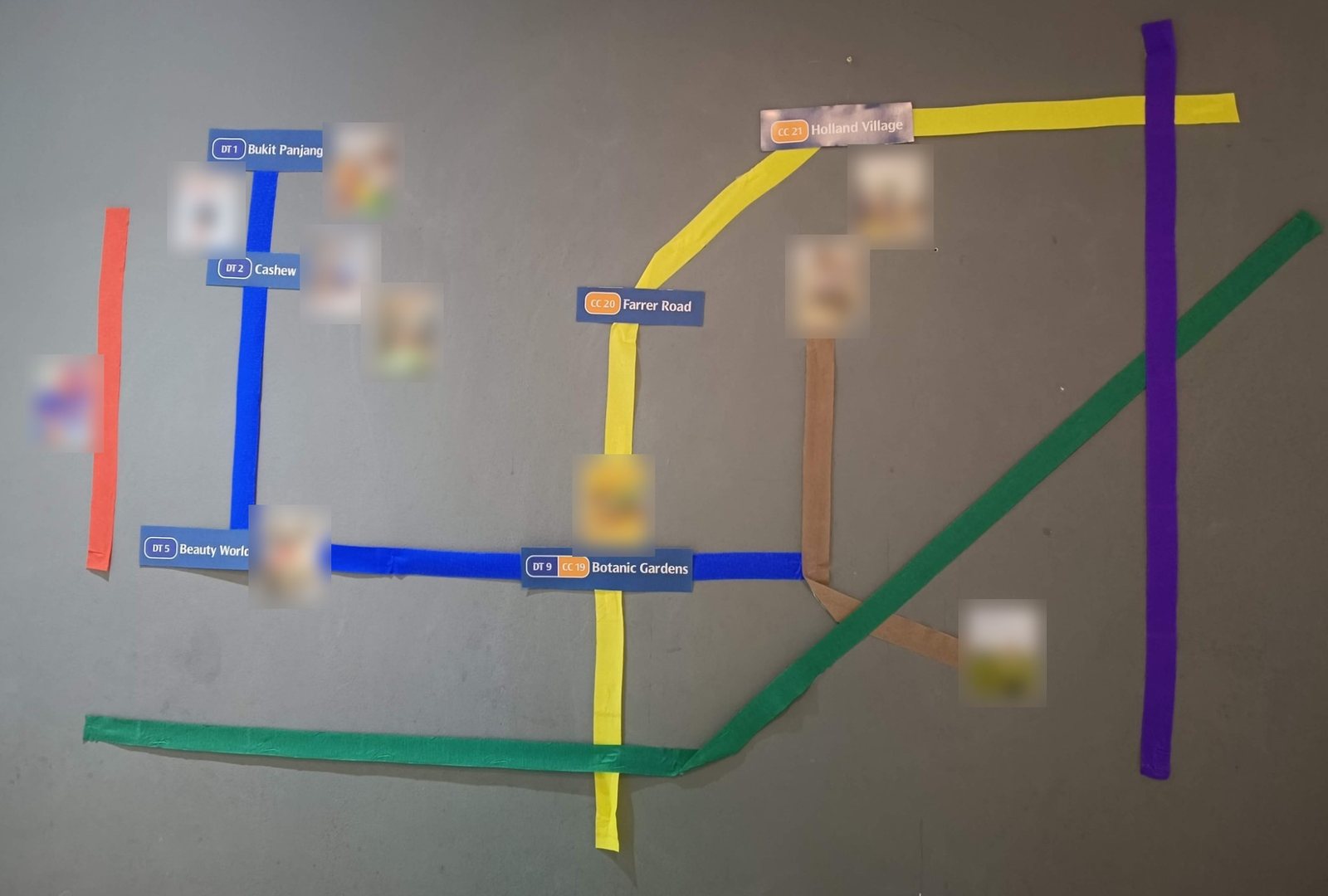 An MRT map made of coloured tape on a grey wall, with station signs for Bukit Panjang, Cashew, Beauty World, Botanic Gardens, Farrer Road and Holland Village, and small photos next to each station
